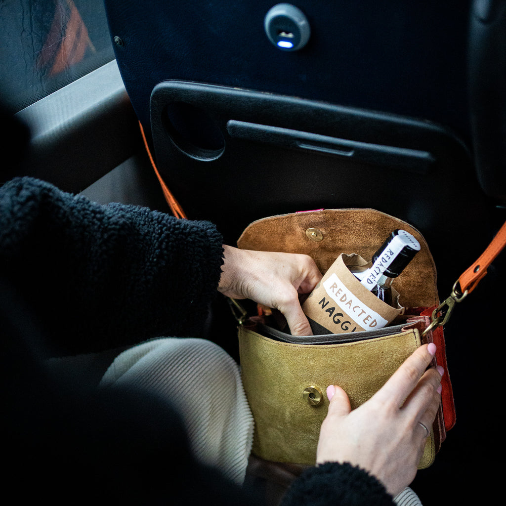 A Redacted whiskey naggin being taken from a purse on a bus